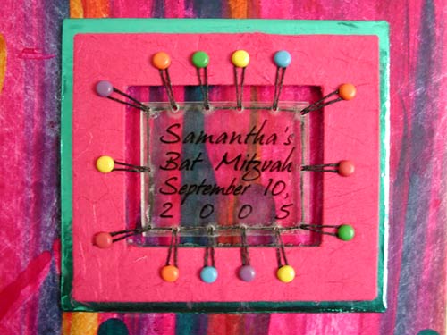 A plexiglas title plate is suspended in a window on the cover of this special bat mitzvah book.